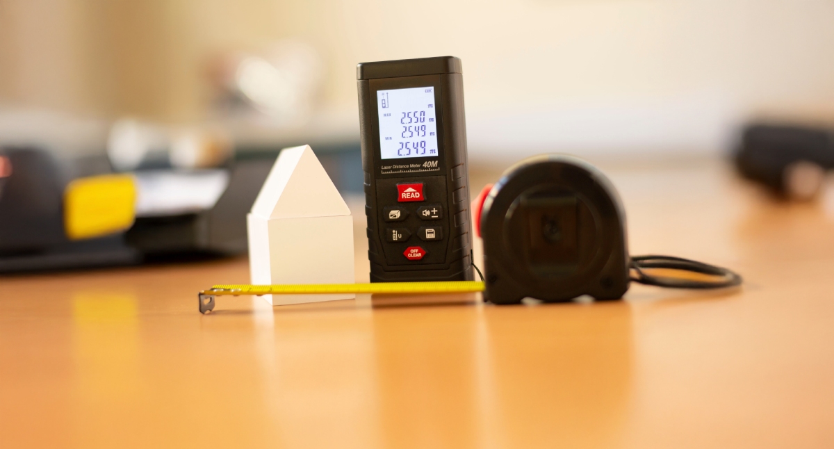 Télémètre laser et mètre ruban à côté d’une maquette de maison